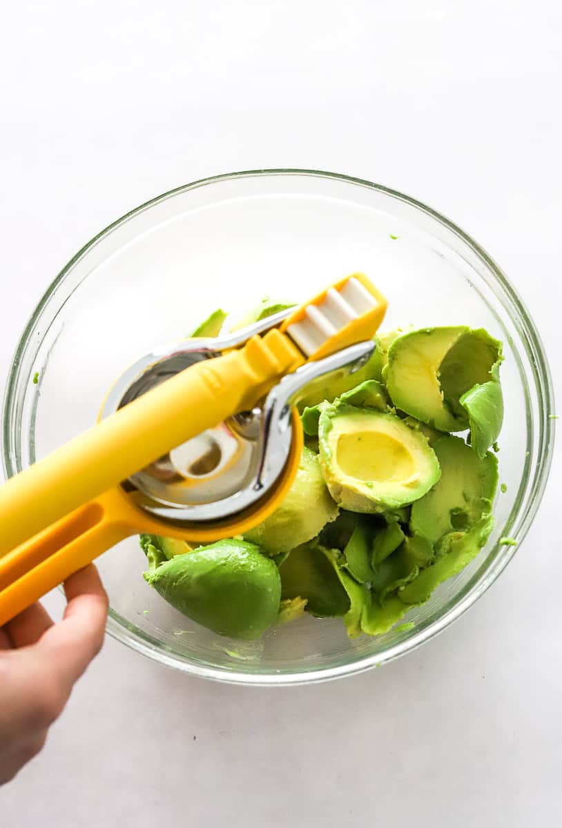 Hand using a juicer to squeeze lime juice onto a bowl of peeled avocados.