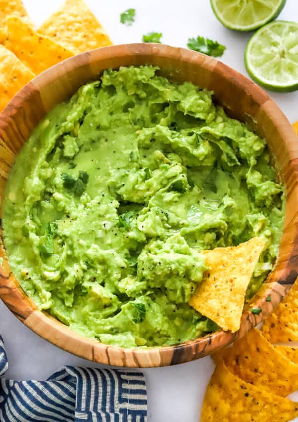 4 ingredient guacamole recipe mixed in a wooden bowl with a tortilla chip in it with more chips behind it.