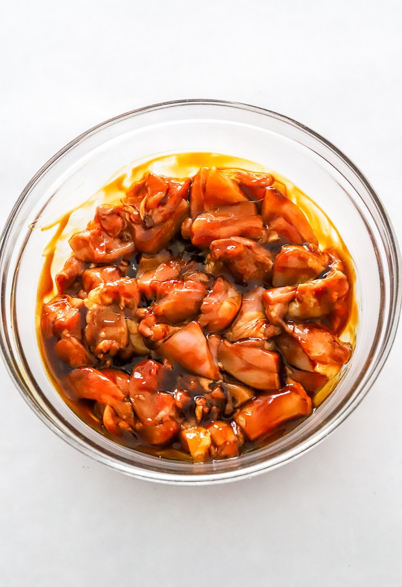 Raw cubed chicken covered in teriyaki sauce in a glass mixing bowl.