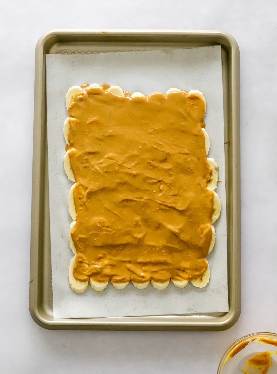 Banana slices arranged in a rectangle shape with creamy peanut butter spread over then on a lined baking sheet.