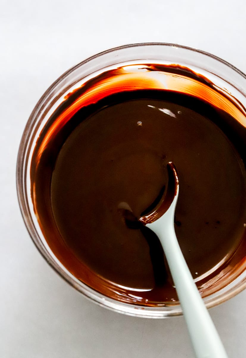Melted dark chocolate in a glass bowl with a rubber spoon in it.