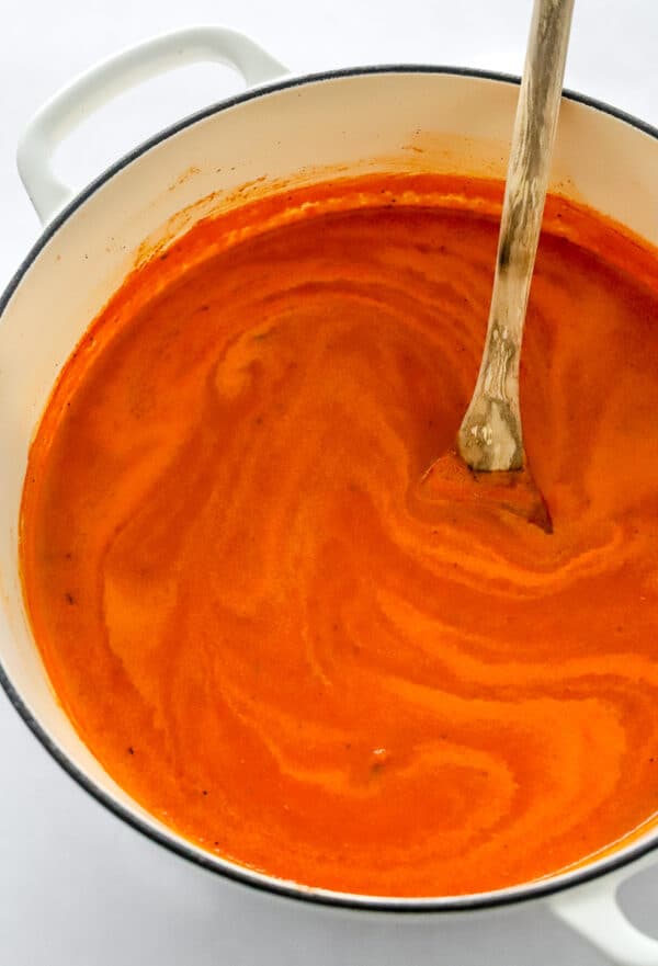 White pot filled with creamy tomato soup with a wooden spoon in the pot.