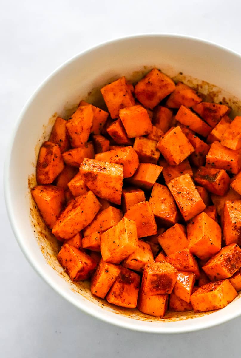 Cubed sweet potatoes in a bowl seasoned with oil, and spices. 