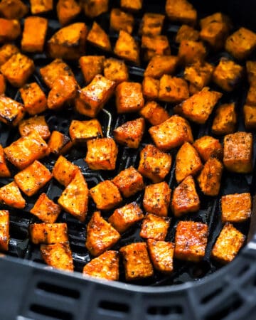 Cubed cooked air fryer sweet potato cubes in a black air fryer basket.