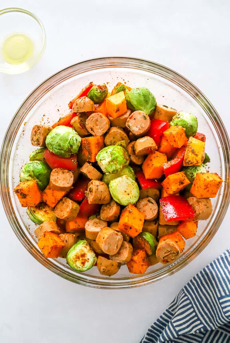Bowl of seasoned veggies and sliced sausage in a glaze mixing bowl.