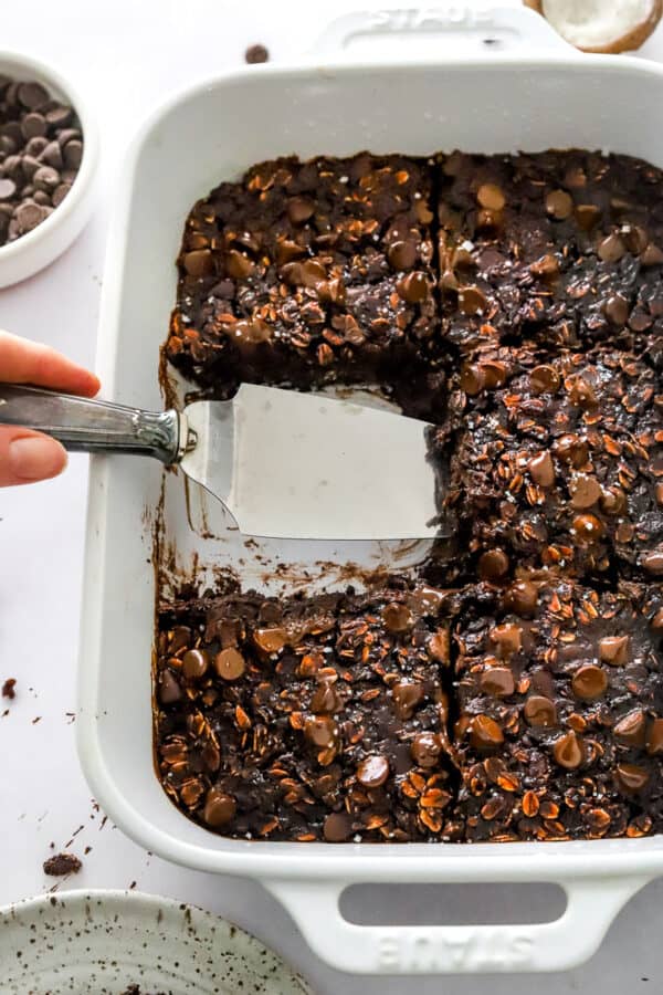 Pan of chocolate oatmeal bake with a serving spoon pulling a slice out of the pan.
