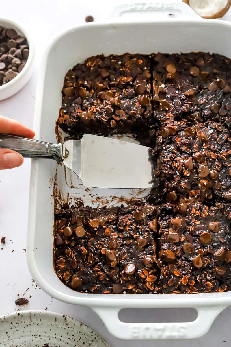 Pan of chocolate oatmeal bake with a serving spoon pulling a slice out of the pan.
