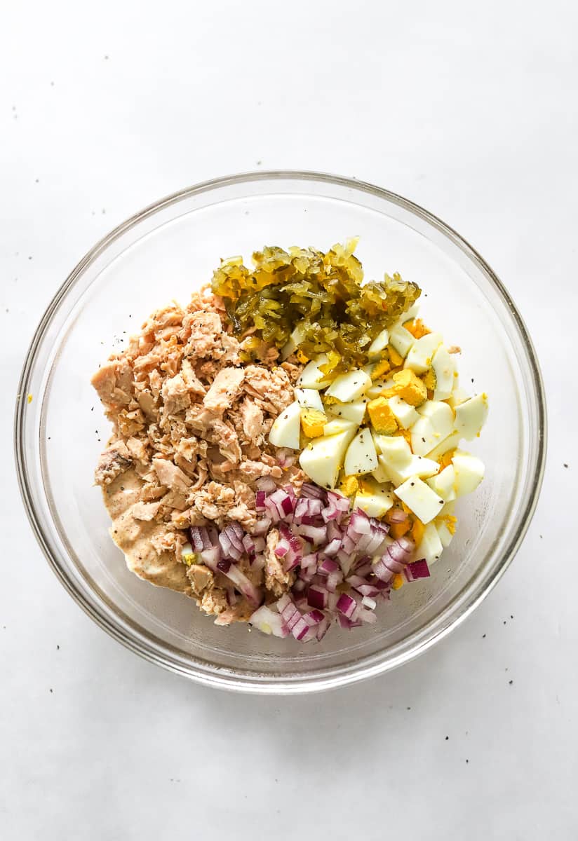 Flaked tuna, chopped hard boiled eggs, chopped red onion, relish and dressing in a glass mixing bowl. 