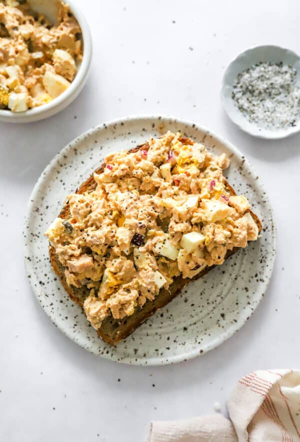 Tuna salad spread on toast on a plate with more in a bowl behind it.