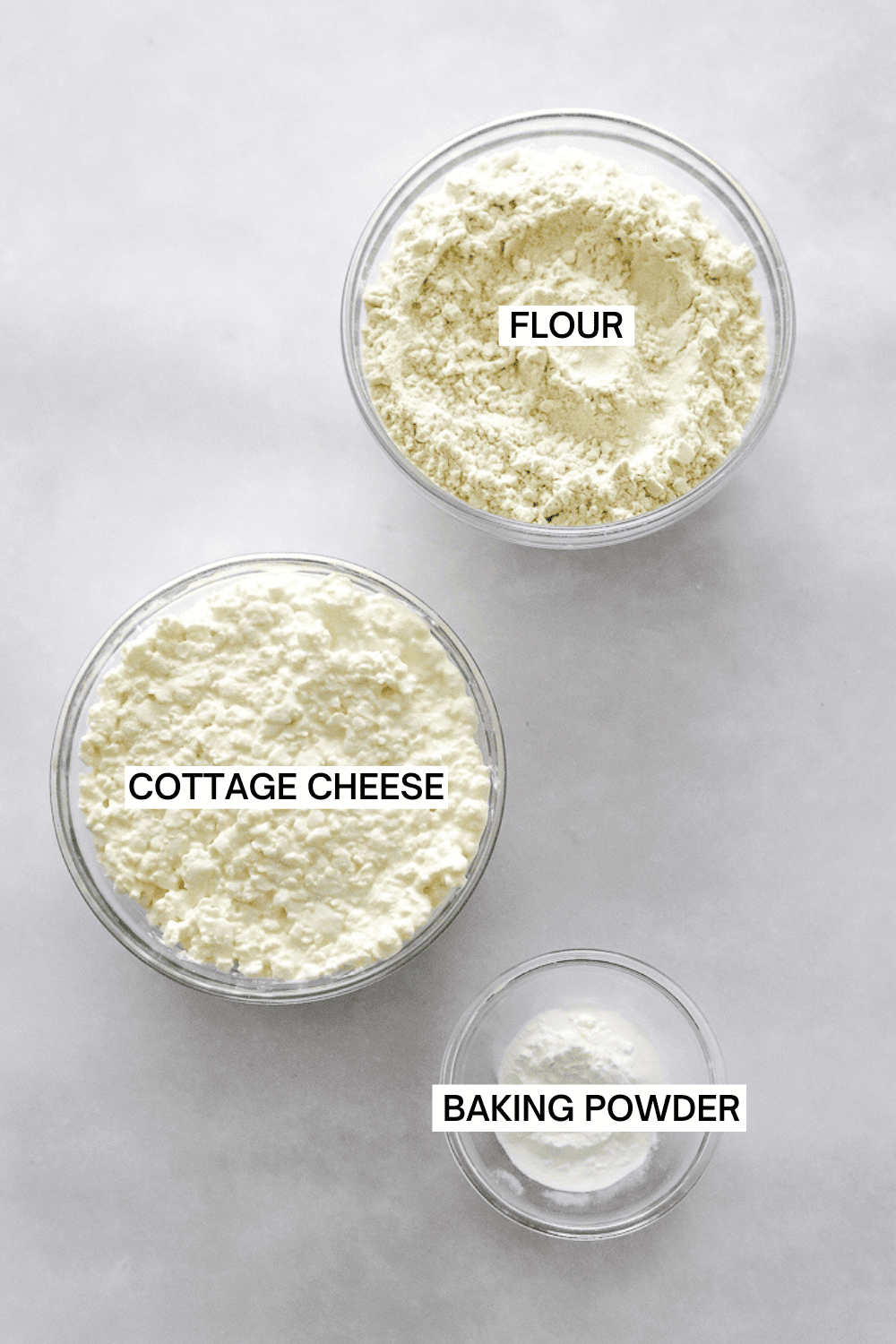 Flour, cottage cheese and baking powder in separate bowls with labels over each of them.