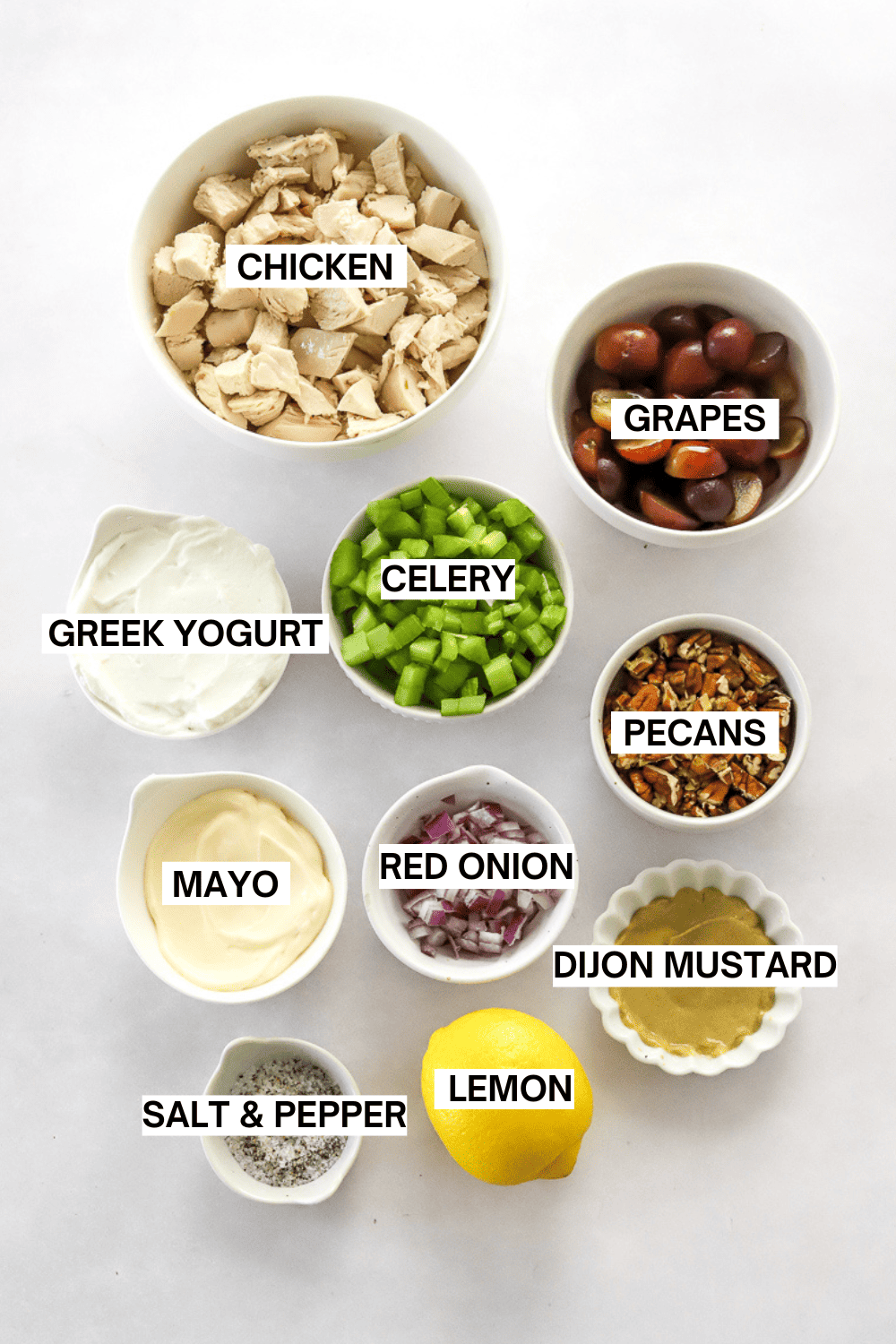 Ingredients for chicken salad in bowls with labels over each ingredient.