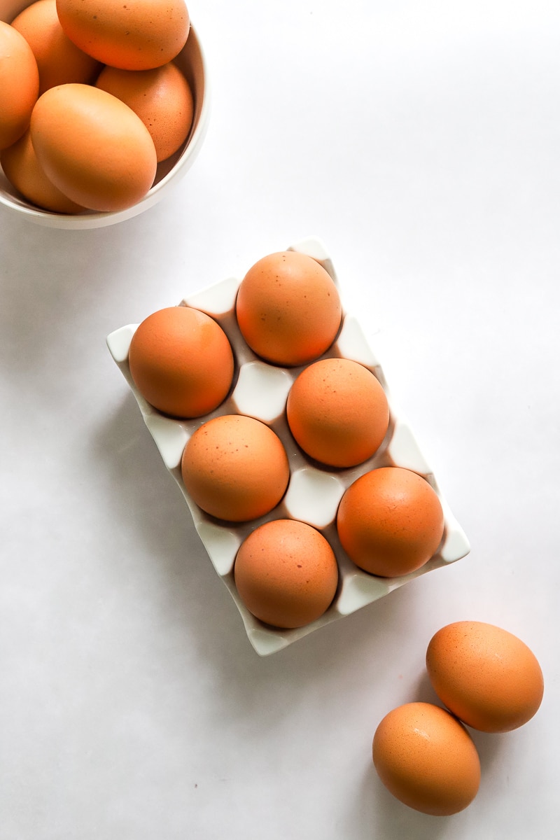 Whole eggs in an egg holder with more in front of them and behind them.