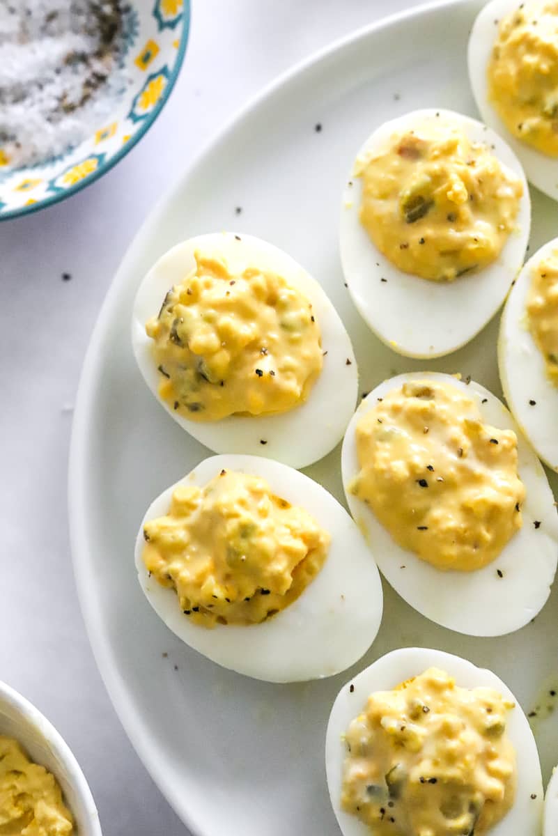 A few deviled eggs on a white plate with a bowl with salt and pepper in it behind it.