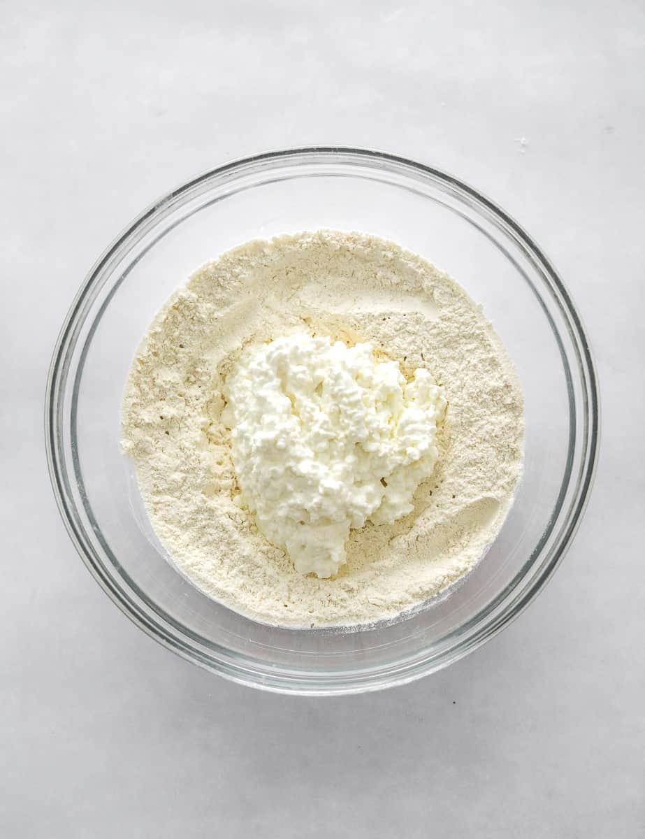 Flour and cottage cheese in a glass mixing bowl.