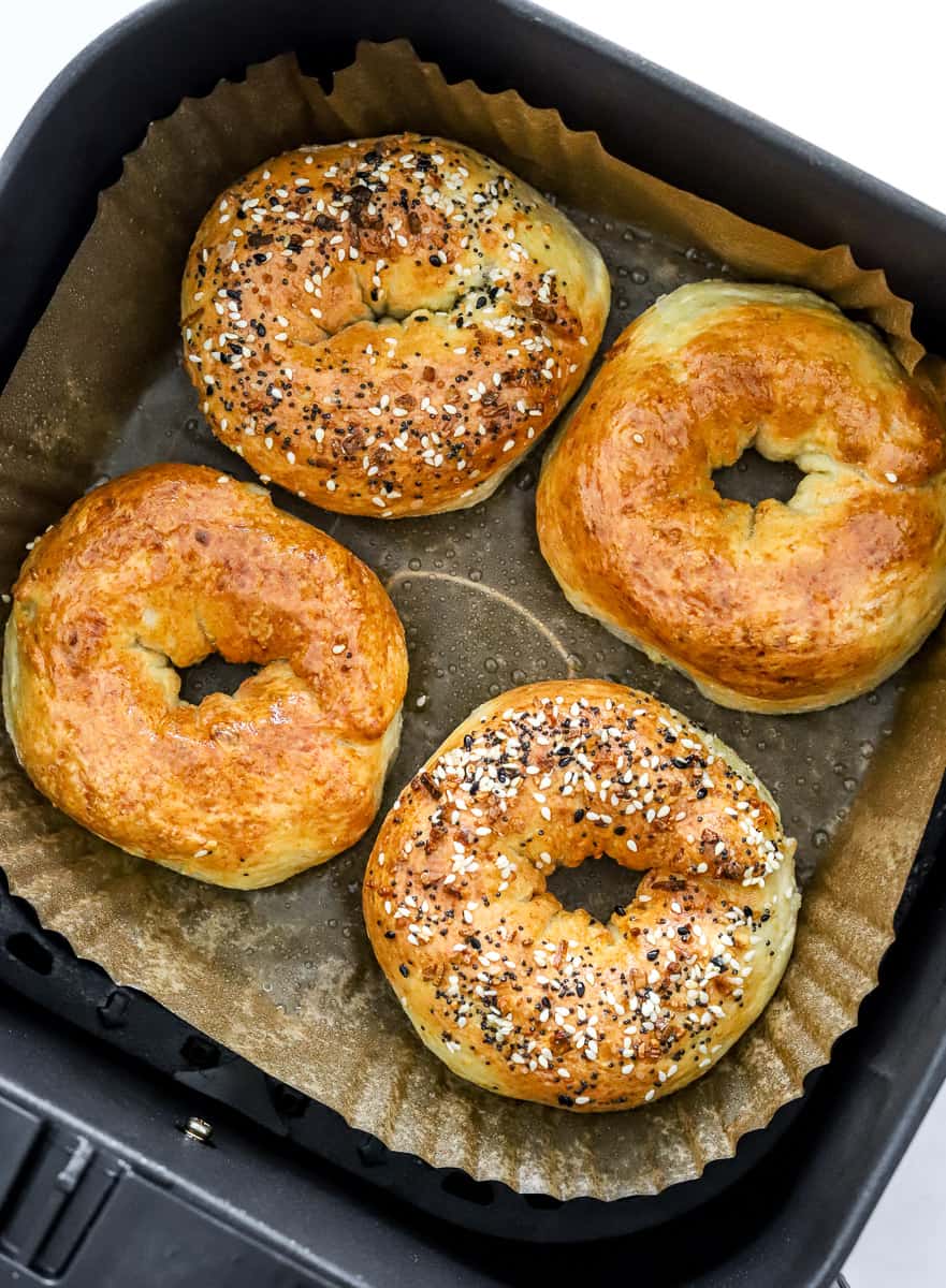 Cooked golden bagels on in a parchment paper lined air fryer basket.