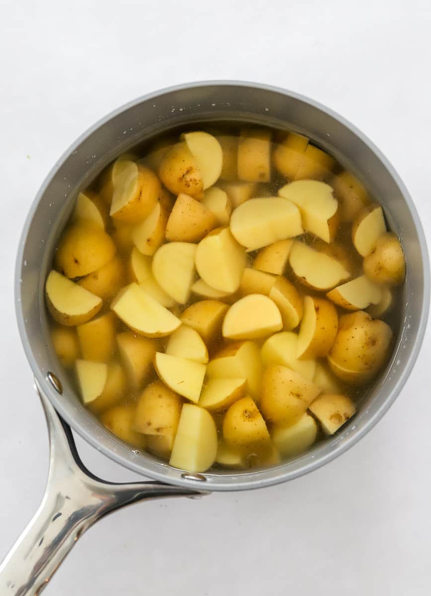 Chopped potatoes covered with water in a silver pot.