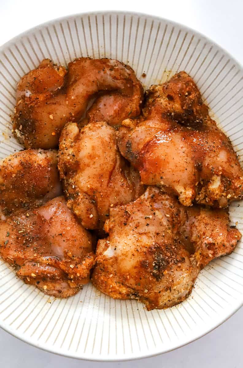Uncooked, seasoned skinless chicken in a round bowl.