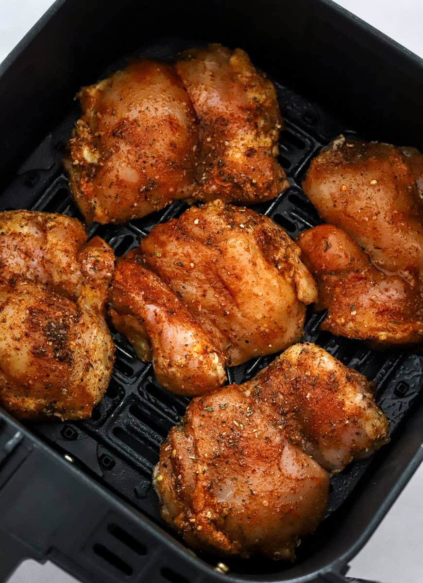 Raw, seasoned boneless skinless chicken thighs in a black air fryer basket.