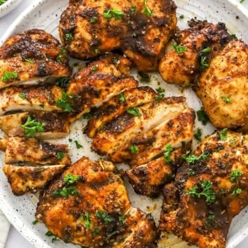 Cooked boneless chicken thighs on a round white plate topped with chopped parsley with more parsley in a bowl behind it.