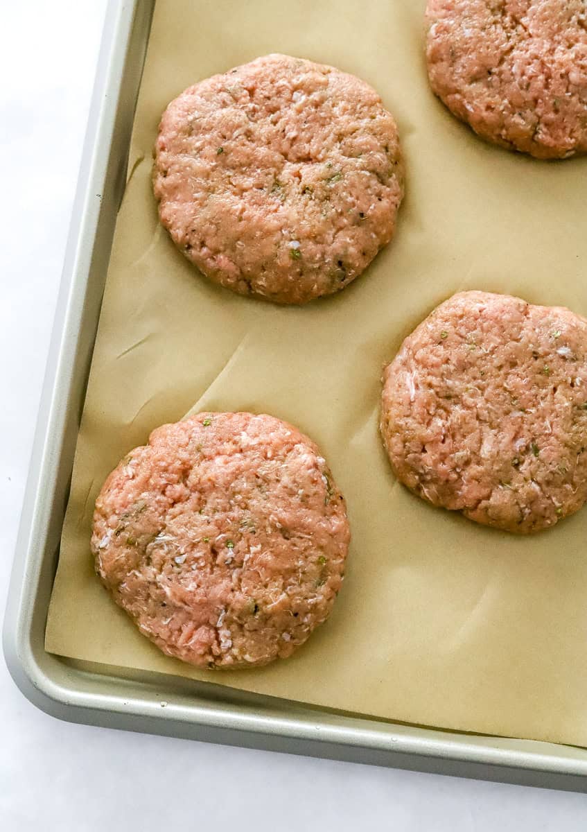 Uncooked formed turkey burger patties on a brown parchment paper lined pan.