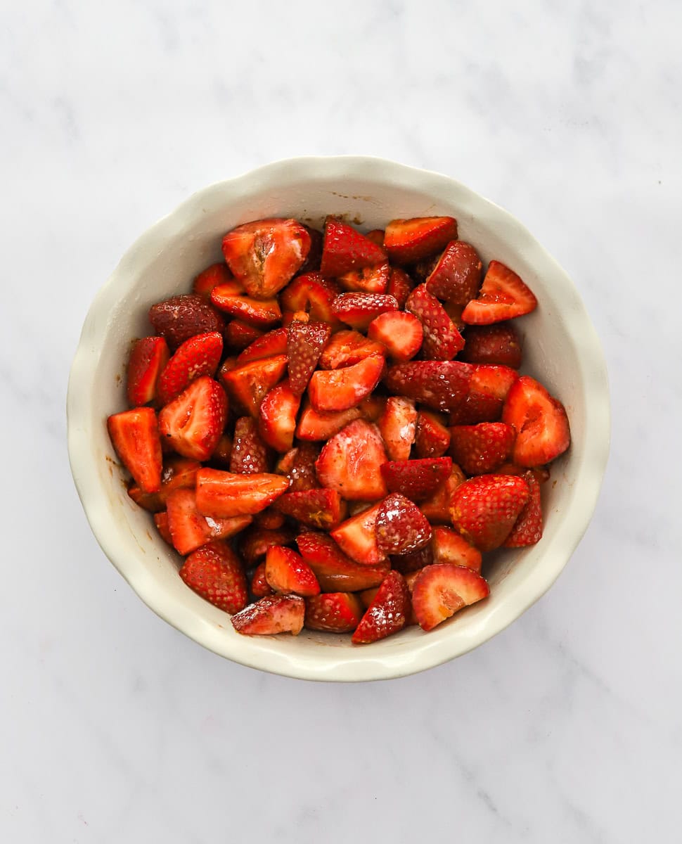 Coated sliced fresh strawberries in a white pie dish.
