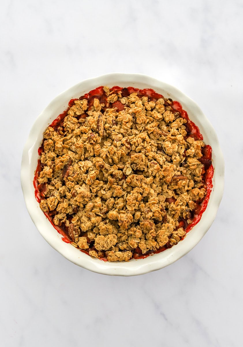 Baked strawberries toped with an oatmeal crumble in a white pie dish.