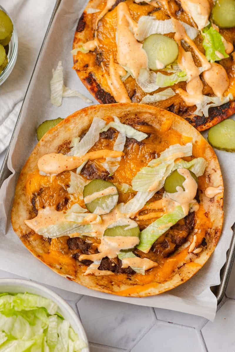 Cheeseburger tacos on tortillas topped with pickles, lettuce and smash burger sauce. 