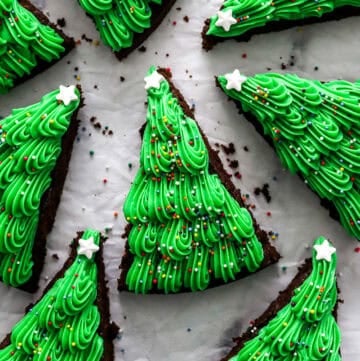 Several Christmas tree brownies decorated like Christmas trees on top of white parchment paper.