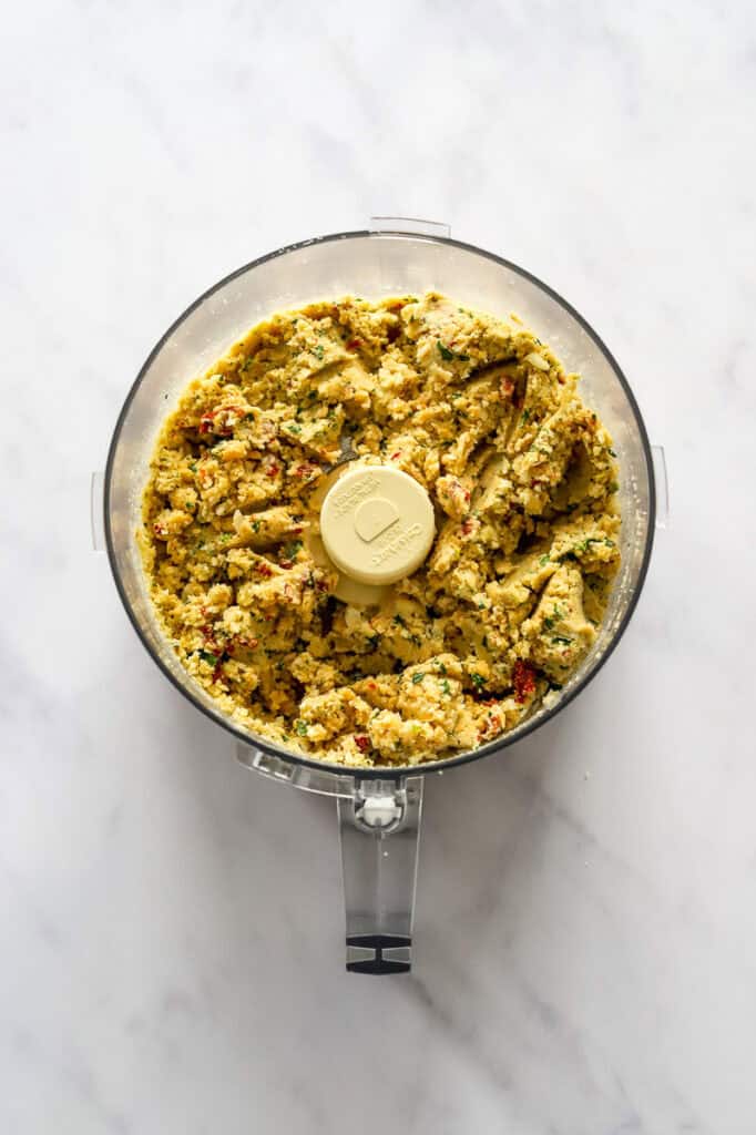 Blended chickpeas, cauliflower and herbs in the bowl of a food processor. 