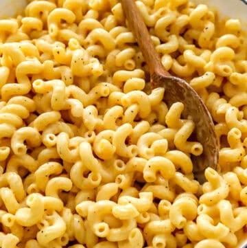 Cheesy cottage cheese Mac and cheese in a white pan with a wood spoon in it and a blue and white towel in front of it.