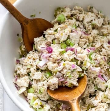 Mixed chicken salad in a white bowl with wooden serving spoons in the bowl.