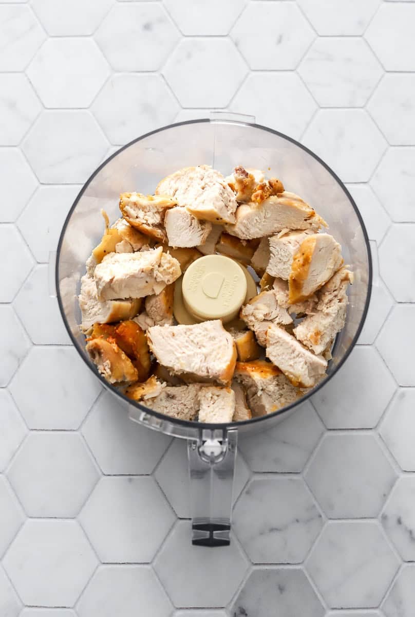 Cooked cubed rotisserie chicken in bowl of a food processor.
