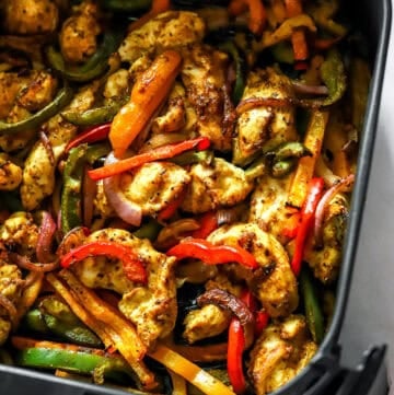 Cooked chicken fajitas in an air fryer basket.