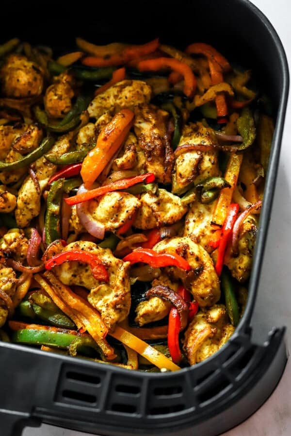 Cooked chicken fajitas in an air fryer basket.