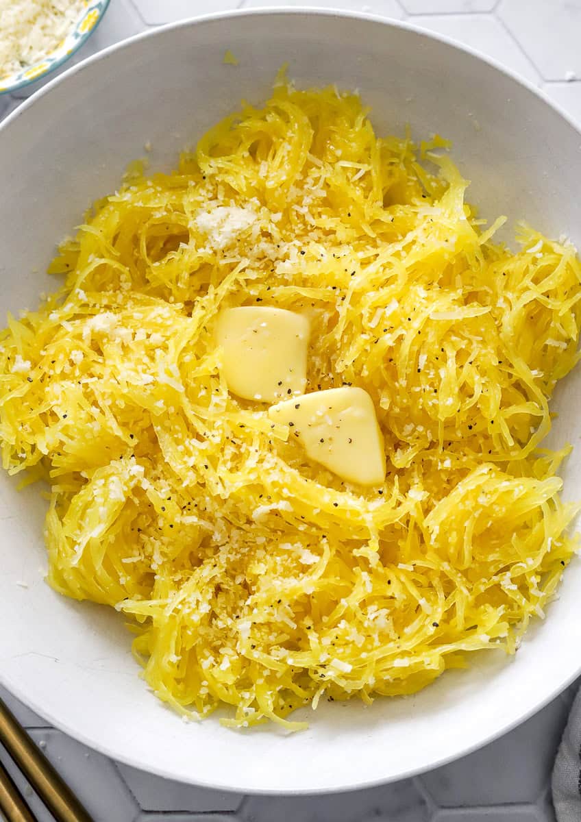 Bowl of cooked yellow squash topped with slabs of butter and parmesan cheese.