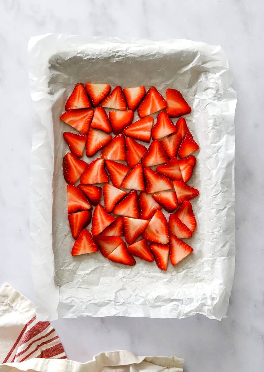 Cut strawberries in rows on a lined baking sheet.