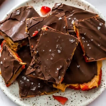 Layered bark bars with strawberries on a white plate with brown specks with more behind it.
