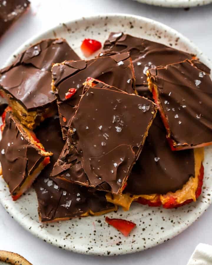 Layered bark bars with strawberries on a white plate with brown specks with more behind it.