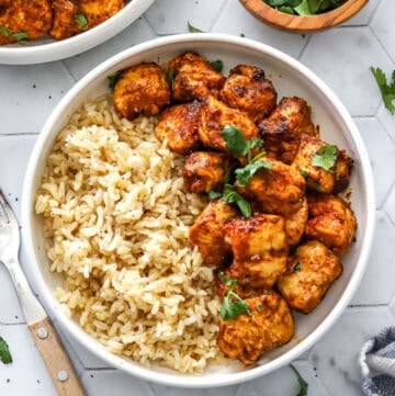 Bowl filled with cooked rice and unbranded air fryer chicken bites with parsley on them, with another bowl of it behind it.
