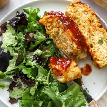 Cooked meatloaf with salad on a with plate with a fork.