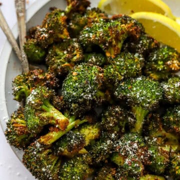 Plate of roasted broccoli with forks and sliced lemon on the plate with it.