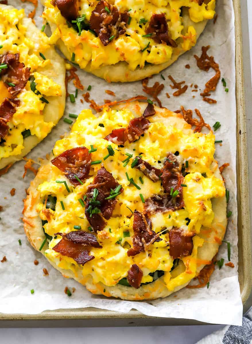Cooked egg and bacon pizzas on a lined baking sheet.