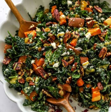 Kale sweet potato salad in a bowl with wood salad spoons in it.