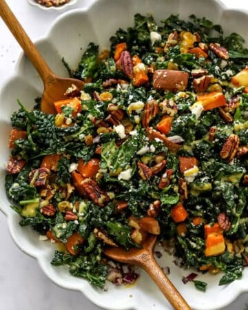 Kale sweet potato salad in a bowl with wood salad spoons in it.