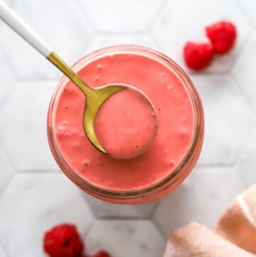 Jar of raspberry vinaigrette with a spoon lifting out of it.