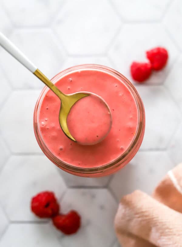 Jar of raspberry vinaigrette with a spoon lifting out of it.