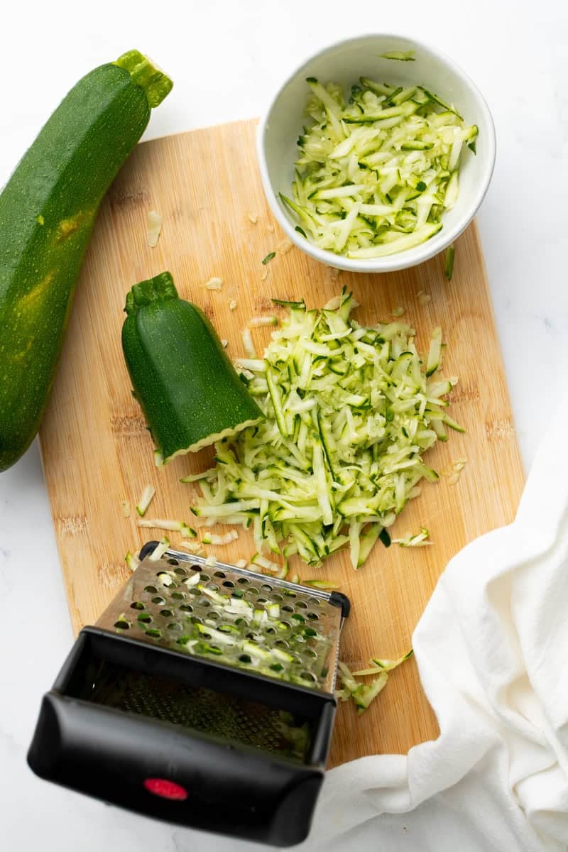 Shredded zucchini on wood cutting board with whole zucchini on it as well. 