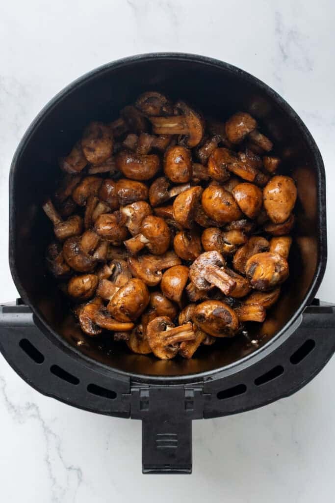 Seasoned uncooked mushrooms in air fryer basket.