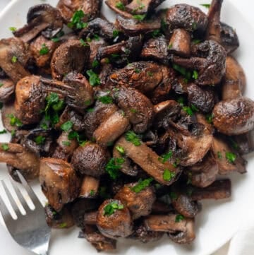 Plate of air fryer mushrooms with a fork on the plate and bowl of parsley behind it.
