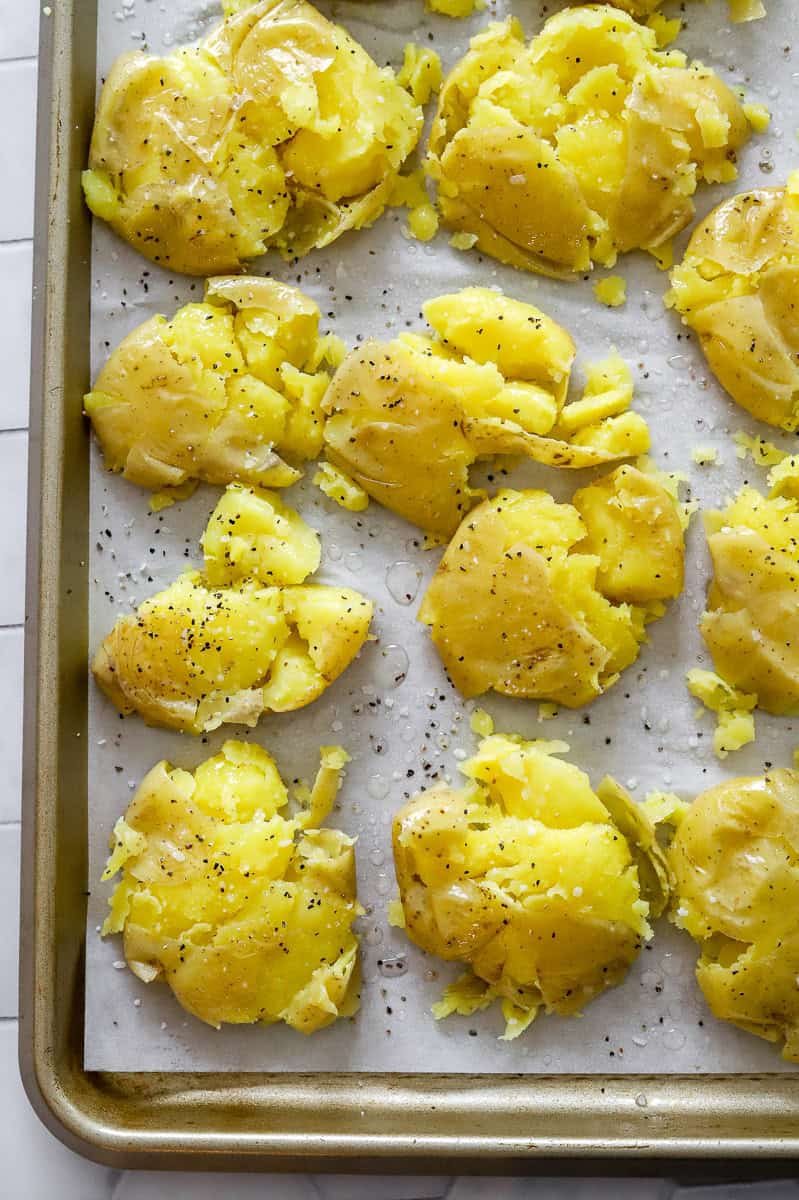 Cooked smashed potatoes on a lined baking sheet.